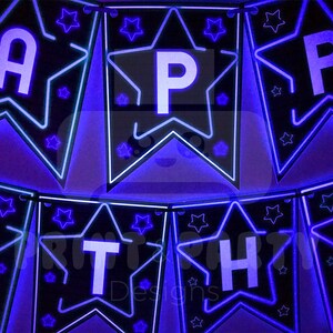 May include: A black and blue star-shaped banner with the word "Happy Birthday" spelled out in white letters. Each letter is on a separate star. The banner is lit up with blue lights.