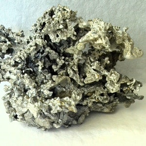 May include: A large, gray, aluminum sculpture with a rough, textured surface. The sculpture is shaped like a rock or a mountain and has many intricate details.