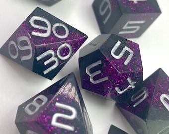 Può includere: Un set di sette dadi poliedrici con base nera e glitter viola. I numeri sono in argento. Include un D20, D12, D10, D8, D6 e due D4. Perfetto per i giochi da tavolo.