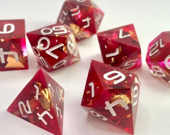 May include: A collection of seven polyhedral dice in different shapes. The dice are a translucent red with gold flakes and white numbering. Suitable for tabletop games, the set includes a d4, d6, d8, d10, d12, d20, and a percentile die.