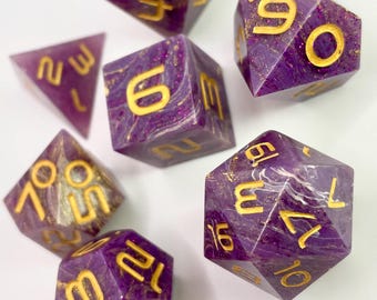 Può includere: Un set di sette dadi poliedrici di varie forme. I dadi sono di un viola intenso con numeri e vortici color oro. I dadi sono per giochi da tavolo.