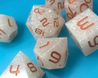 Può includere: Set di sei dadi bianchi con numeri color rame. I dadi sono realizzati in un materiale scintillante e hanno una varietà di forme, tra cui un d4, d6, d8, d10, d12 e d20.