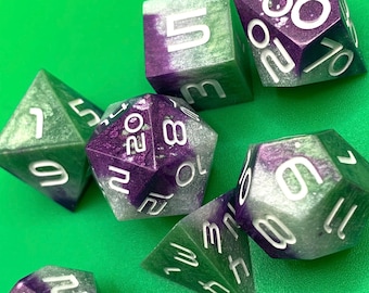 Può includere: Set di sei dadi verdi e viola con numeri bianchi. I dadi sono fatti di un materiale traslucido con una finitura scintillante.
