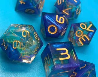 Può includere: Set di sei dadi blu e verdi con glitter dorati e numeri dorati. I dadi sono su uno sfondo blu.