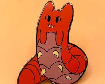 May include: Red and purple enamel pin of a cartoon monster with sharp teeth and a curled tail.