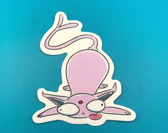 Può includere: Un adesivo di cartone animato rosa e bianco di un personaggio Pokemon con occhi grandi e la lingua che sporge. Il personaggio è capovolto con la coda arrotolata.