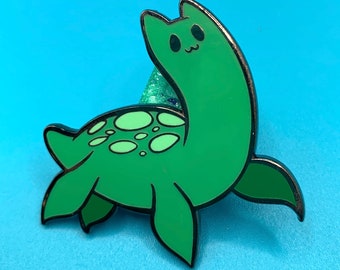 May include: Green enamel pin of a cartoon sea monster with a long neck and a cute face. The monster has a shell with light green spots.