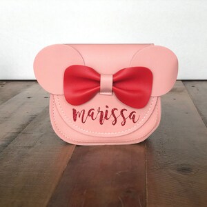 May include: A pink faux leather purse with a red bow and the name "marissa" written in red glitter.