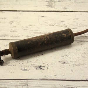 May include: A vintage metal hand pump with a black finish and a long, thin nozzle. The pump has a T-shaped handle with three round knobs.