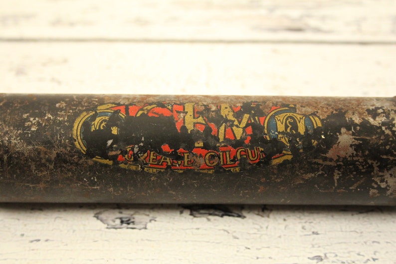 May include: A vintage metal container with a faded label that reads "Grease Oil Cup". The container is rusty and has a black background with gold and red lettering.