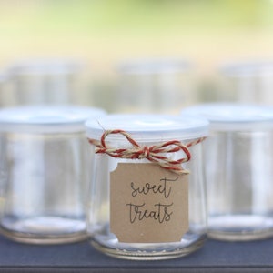 Puede incluir: Seis tarros de vidrio transparentes con tapas blancas, uno atado con cuerda y una etiqueta marrón que dice "sweet treats".