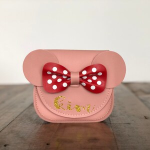May include: A pink faux leather purse with a red and white polka dot bow and the name "Kimi" written in gold glitter.