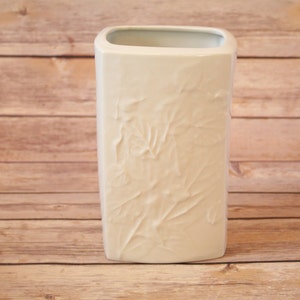 May include: White ceramic vase with an embossed floral design. The vase has a rectangular shape and a smooth, glossy finish.