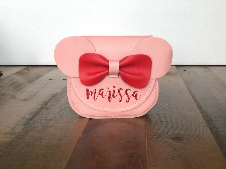 May include: A pink faux leather purse with a red bow and the name "marissa" written in red glitter.