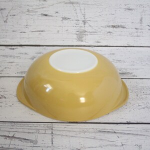 May include: A yellow ceramic mixing bowl with a white interior. The bowl has a rounded shape and a smooth, glossy finish.