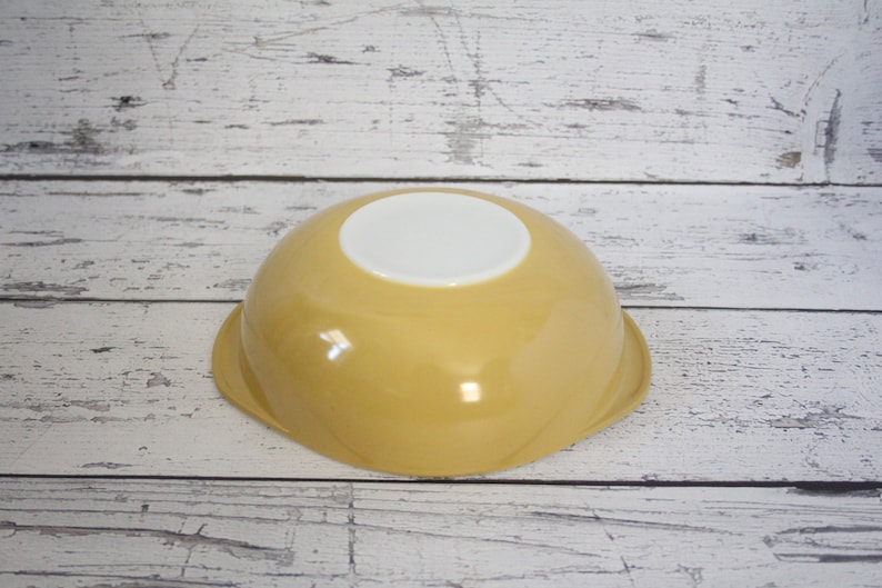 May include: A yellow ceramic mixing bowl with a white interior. The bowl has a rounded shape and a smooth, glossy finish.