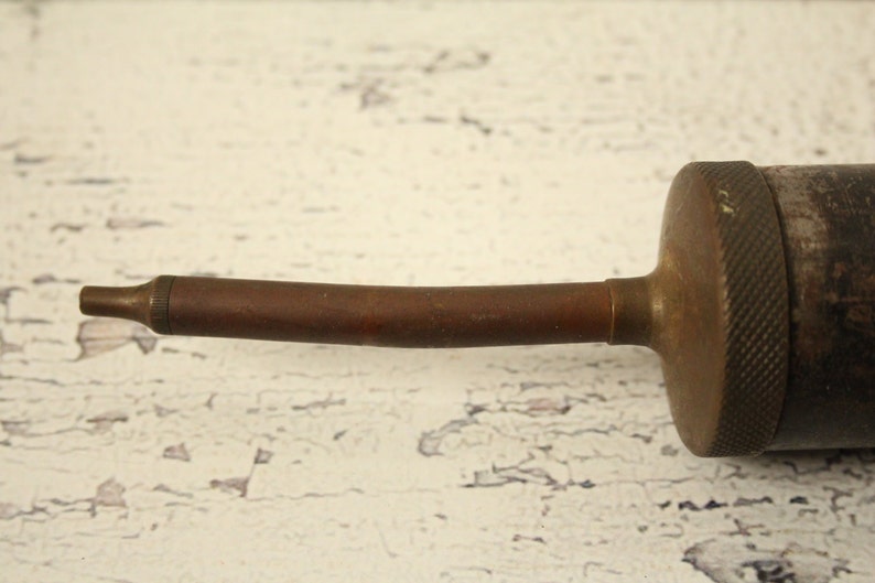 May include: A vintage oil can with a long, curved spout. The can is made of metal and has a worn, brown finish.