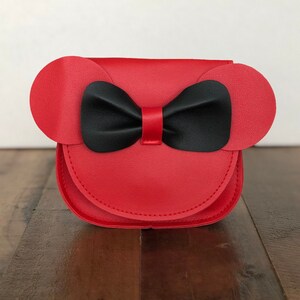 May include: A red faux leather purse with black bow and ears. The purse is shaped like a cartoon character's head.