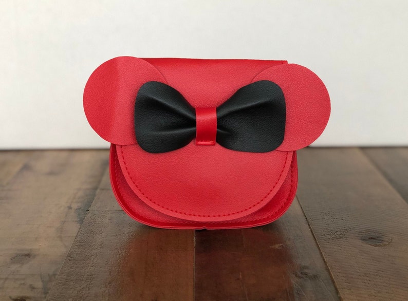 May include: A red faux leather purse with black bow and ears. The purse is shaped like a cartoon character's head.