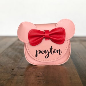 May include: A pink faux leather purse with a red bow and the name "peyton" written in black.