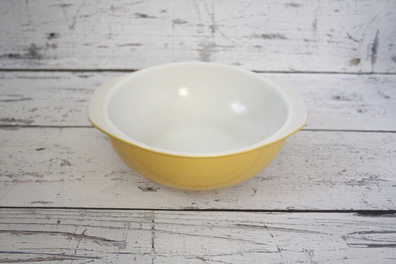 May include: A yellow mixing bowl with white interior. The bowl has two handles on the sides.