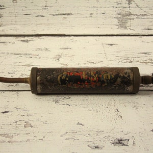May include: A vintage metal grease gun with a black handle and a long, thin nozzle. The gun has a black and red label with the text "The Perfect Grip".