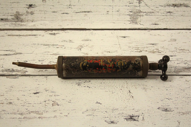 May include: A vintage metal grease gun with a black handle and a long, thin nozzle. The gun has a black and red label with the text "The Perfect Grip".
