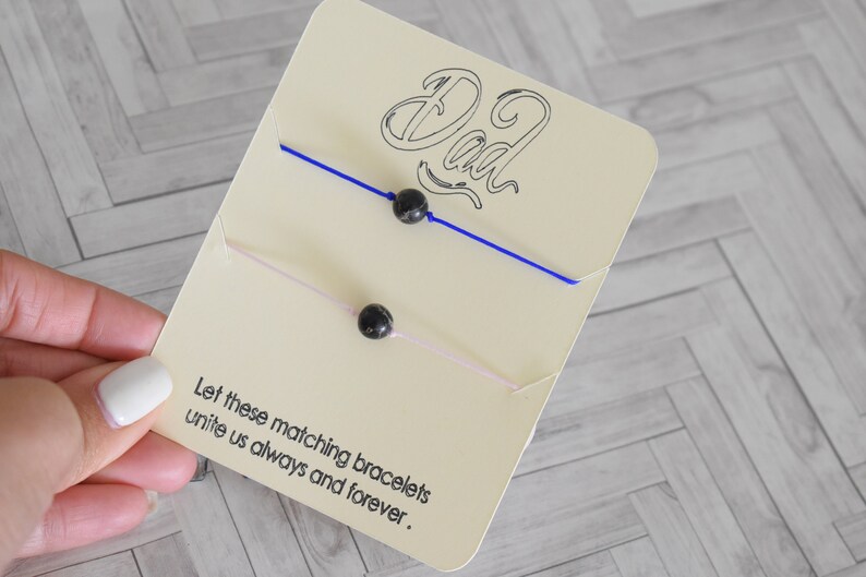 May include: Two matching bracelets with black beads on a card that says "Dad" and "Let these matching bracelets unite us always and forever."
