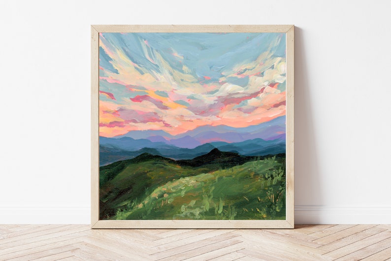Puede incluir: Una pintura de un paisaje de monta&ntilde;a con un cielo rosa y azul. Las monta&ntilde;as son verdes y azules, y el cielo est&aacute; lleno de nubes. La pintura est&aacute; enmarcada en un marco de madera claro.