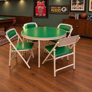 May include: A round table with a green top and white metal frame, accompanied by four matching folding chairs. Each chair features a white metal frame with a green padded seat and backrest, arranged around the table on a wooden floor.