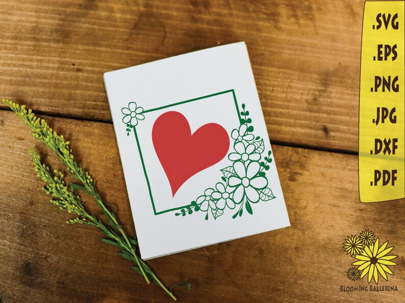 May include: A white card with a green frame and a red heart inside. The frame is decorated with white flowers and green leaves.