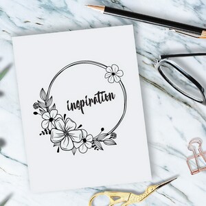 May include: A white card with a black floral wreath and the word "inspiration" written inside the wreath.