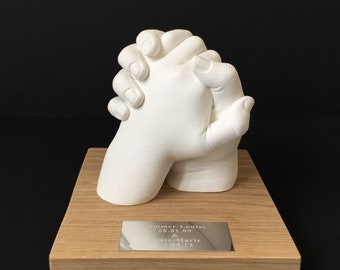 May include: White plaster hand cast of two hands clasped together on a wooden base with a silver plaque that reads "Summer-Louise 28.01.09 & Indie-Marie 5.08.12"
