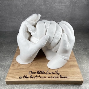 Peut inclure: Sculpture en plâtre blanc d'empreintes de mains d'une famille se tenant la main, montée sur un socle en bois avec l'inscription "Notre petite famille est la meilleure équipe que nous puissions avoir."