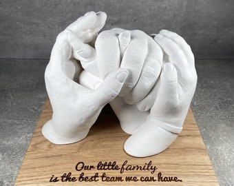 May include: White plaster handprint sculpture of a family holding hands, mounted on a wooden base with the inscription "Our little family is the best team we can have."