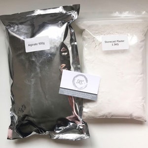 Könnte beinhalten: Zwei weiße Beutel mit Pulver, einer mit der Aufschrift "Alginat 900g" und der andere mit der Aufschrift "Steinabgussgips 1.5KG".