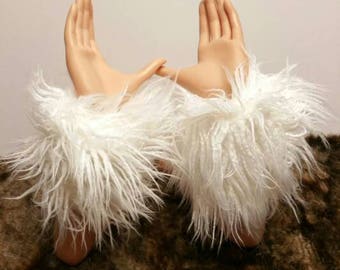May include: Two white faux fur arm warmers with shaggy texture. The arm warmers are shown on a pair of mannequin hands, with the hands raised in a gesture of holding something.