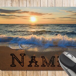 May include: A mouse mat featuring a sunset over the ocean with waves breaking on the beach. The word "NAME" is written in the sand.