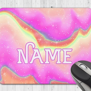 May include: A personalised mouse mat featuring a colourful pink, orange, and rainbow watercolour design. The word "NAME" is displayed in a white, outlined font. A black and silver computer mouse is in the corner.