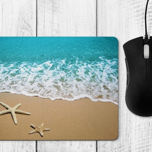 May include: A blue and white beach scene with two starfish on a sandy beach. The mouse mat is ideal for adding a touch of the beach to your desk.