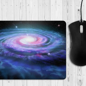 May include: A mouse mat featuring a swirling galaxy with a pink and blue nebula at its centre. The galaxy is surrounded by a dark blue background with scattered stars.