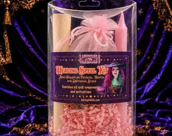 May include: A clear plastic box containing a Healing Spell Kit with a pink candle, a rolled parchment scroll, and a pink organza pouch nestled in pink shredded paper. The label features an illustration of a person and the text Healing Spell Kit.