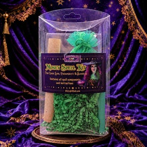 May include: A clear plastic box containing a Money Spell Kit with a label featuring a person in a witch hat, green shredded paper, a cork-topped tube, and a green organza bag. The label reads Money Spell Kit For Good Luck, Prosperity & Success.