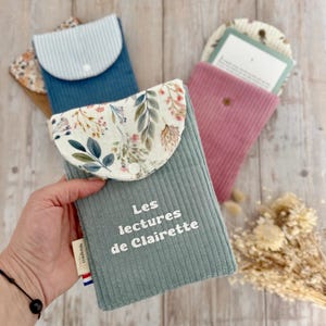 Peut inclure: Plusieurs pochettes à livres en velours côtelé, dans des tons de bleu et de rose. La pochette avant porte le texte "Les lectures de Clairette" en blanc. Chaque pochette a un rabat à motifs et une fermeture à bouton. Idéal pour protéger les livres.