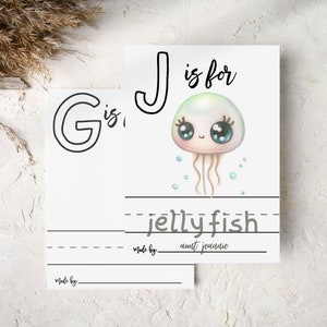 Blank baby shower coloring pages G and J. Letter J page shows a sample drawing of a jellyfish and is signed by a guest