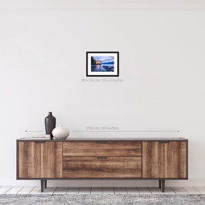 May include: A framed photograph of a lake with a building on the shore. The building is lit up with warm light, and the water is a deep blue. The sky is a soft pink and purple. The photo is 12 inches by 8 inches.