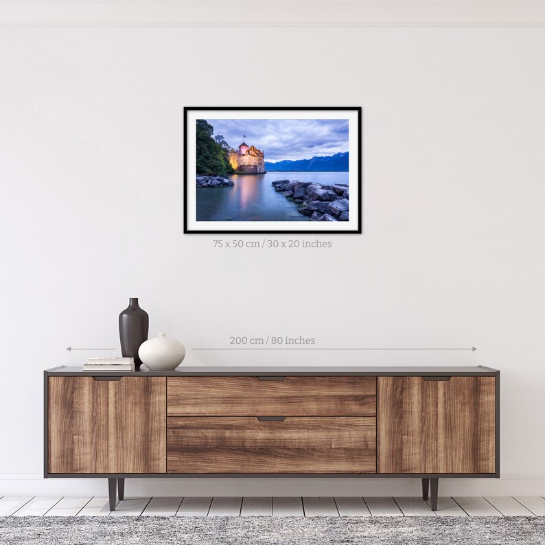 May include: A framed photograph of a castle on a lake at dusk. The castle is lit up with warm lights, and the water is a deep blue. The sky is a soft pink and purple. The photo is 30 inches by 20 inches.