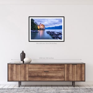 May include: A photograph of a castle on a lake at dusk. The castle is lit up and the water is calm. The sky is a soft blue and purple. The image is 36 x 24 inches.