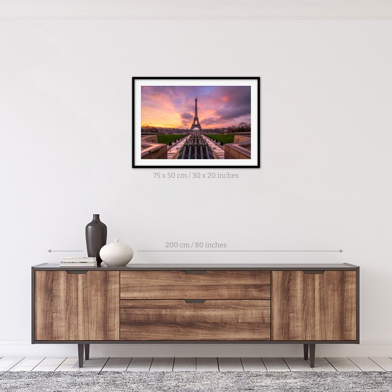 Puede incluir: Fotograf&iacute;a enmarcada de la Torre Eiffel al atardecer. La imagen, de 75 x 50 cm, captura el emblem&aacute;tico monumento contra un cielo vibrante con tonos de naranja, rosa y morado. La fotograf&iacute;a se exhibe sobre un mueble de madera.