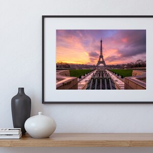Puede incluir: Impresi&oacute;n enmarcada de la Torre Eiffel al atardecer. La ic&oacute;nica torre se alza sobre un cielo vibrante de tonos naranja, rosa y p&uacute;rpura. La imagen est&aacute; enmarcada en negro y se exhibe en una estanter&iacute;a de madera con jarrones.
